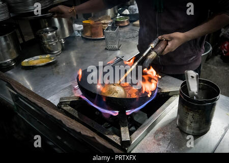 Chef cooking with fire with frying pan. Chef frying food in flaming pan on gas hob. street cafe with street food in India. Stock Photo