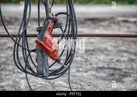 Close-up of a new modern red drill with a long wire wrench attachment hanging ready for work against a building site Stock Photo