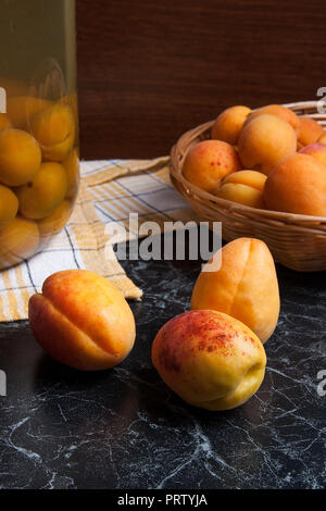 Ripe organic apricots harvested at summer time and big glass jar with canned sweet apricot compote on dark marble. Composition in rustic style - organ Stock Photo