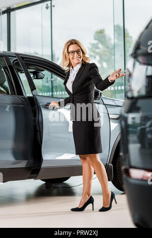 happy female car dealer opening car in showroom Stock Photo