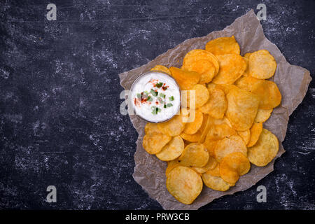 Potato chips with dip on parchment paper. Dark concrete background. Top view Stock Photo