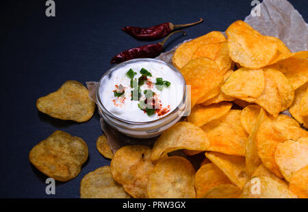 Potato chips with dip on parchment paper. On dark black stone table background Stock Photo
