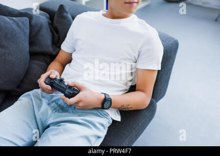 cropped image of asian man playing video game and lying on sofa at home Stock Photo
