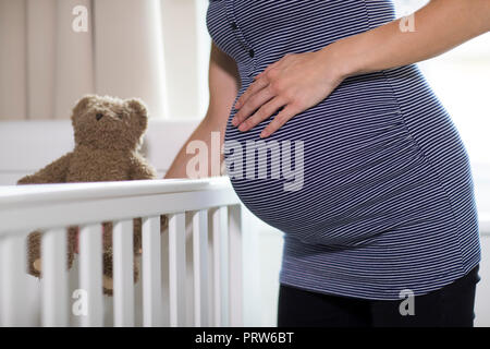 Close Up Of Pregnant Woman Putting Teddy Bear Into Cot In Nursery Stock Photo