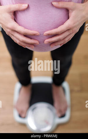 Close Up View Looking Down On Pregnant Woman Standing On Bathroom Scales Stock Photo