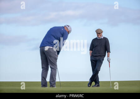 Actor Hugh Grant watches his playing partner Paul McGinley putt out on the 18th green during day one at Kingsbarns Golf Course, St Andrews Stock Photo