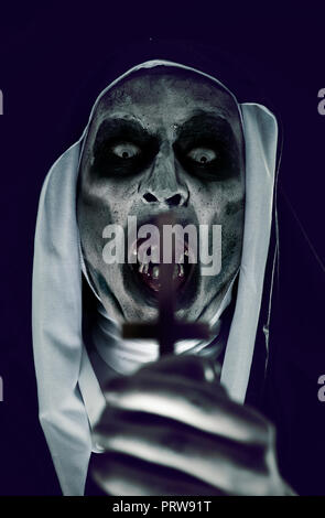 closeup a frightening evil nun, wearing a typical black and white habit, with an upside down cross in her hands Stock Photo