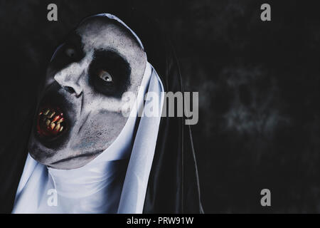 closeup of a frightening evil nun, with bloody teeth and scary eyes, wearing a typical black and white habit, against a dark background, with some bla Stock Photo