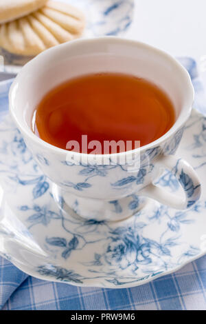 A nice cup of English tea served in traditional fine floral pattern porcelain cup and saucer with defocussed biscuits in the background Stock Photo