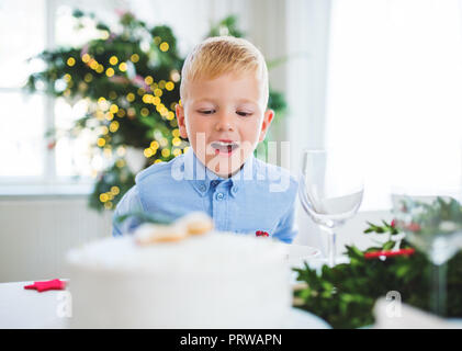 A small boy looking at a cake at home at Christmas time.
