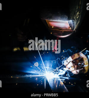 Professional mask protected welder man working on metal welding and sparks metal.