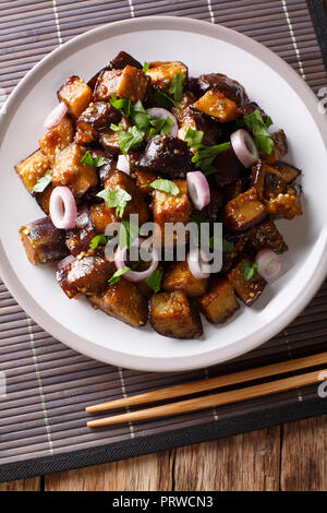 Chinese style eggplants in spicy soy sauce with ginger, garlic, pepper, closeup on a plate on the table. Vertical top view from above Stock Photo