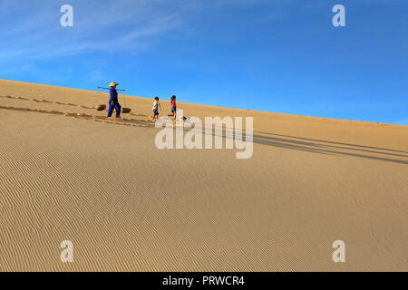 woman carries a bamboo frame on the shoulder and two children walking home across the Mui Dinh sand dunes Ninh Thuan Province Stock Photo