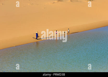 woman carries a bamboo frame on the shoulder and two children walking home across the Mui Dinh sand dunes Ninh Thuan Province Stock Photo