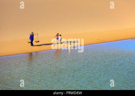 woman carries a bamboo frame on the shoulder and two children walking home across the Mui Dinh sand dunes Ninh Thuan Province Stock Photo