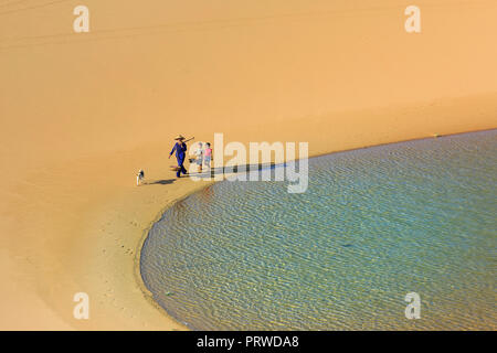 woman carries a bamboo frame on the shoulder and two children walking home across the Mui Dinh sand dunes Ninh Thuan Province Stock Photo