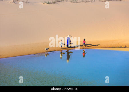 woman carries a bamboo frame on the shoulder and two children walking home across the Mui Dinh sand dunes Ninh Thuan Province Stock Photo