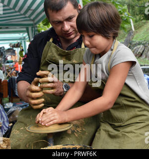 Open-air pottery workshop for children during Etara folk festival. A potter craftsman shows a small girl how to work with clay and pottery wheel Stock Photo