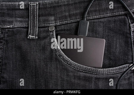 Black portable hard drive with cable in the case lies in the front pocket of black jeans Stock Photo