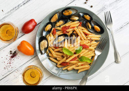 Penne pasta with mussels, tomatoes and white wine on a white wooden rustic background. Top view,flat lay. Mediterranean food