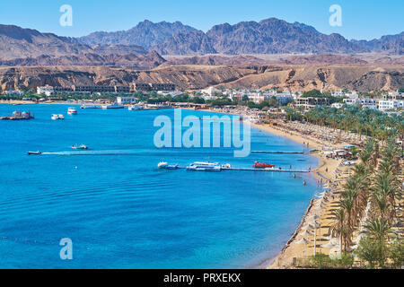 The cozy sand beach of Sharm El Maya is lined with shady palm trees and surrounded by Sinai desert rocks, Sharm El Sheikh, Egypt. Stock Photo