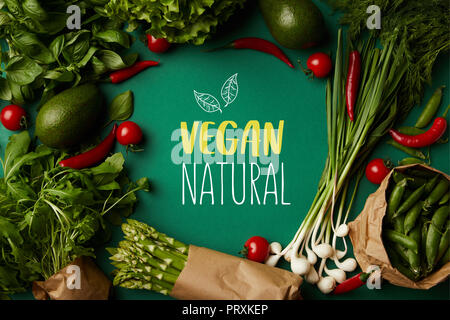 top view of round frame made of various ripe vegetables on green surface with "vegan natural" lettering Stock Photo