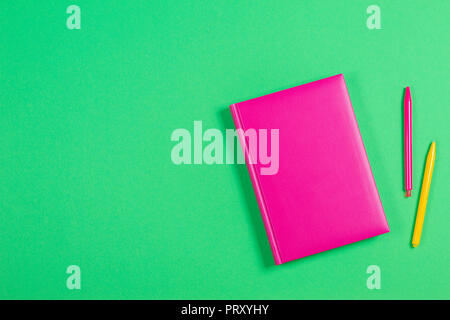 Pink hardcover book and colorful pens on green background Stock Photo