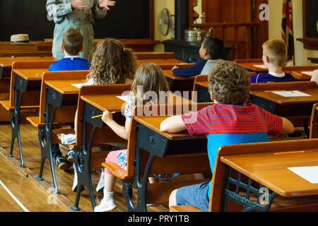 Group of school children sitting at desks and listening to teacher during lesson in classroom. Stock Photo