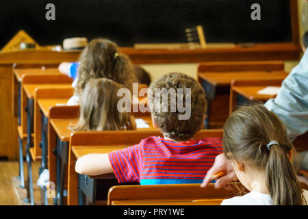 Group of school children sitting at desks and listening to teacher during lesson in classroom. Teacher indicates an error. Stock Photo