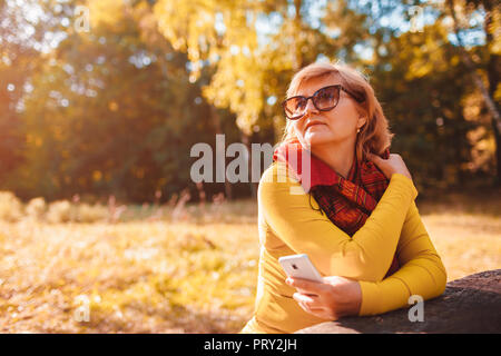Middle-aged woman taking selfie on phone walking in park. Senior lady enjoys nature in autumn forest Stock Photo