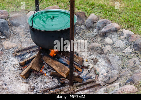 Food pot hangs over burning fire. Stock Photo