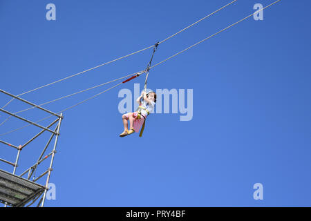 Happily smiling little girl hanging on a zip-line high in the blue sky during the Extreme sports festival autumn 2018 in Sofia City, Bulgaria Stock Photo