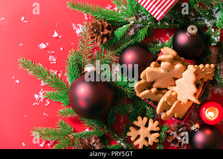 Above view of a box with ginger Xmas cookies, red balls, green fir twigs, on a red background with snowflakes. A Christmas banner or greeting card. Stock Photo
