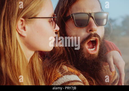 Smiling hipster couple in sunglasses hugging and having fun outdoors in sunrise. Bearded man and blond woman. Stock Photo