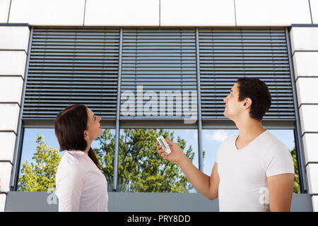 Couple Standing Outside Modern Building Using Remote To Open Window Shutter Stock Photo