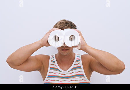 A handsome guy looks through rolls of toilet paper and simulating binoculars. Finding solutions to health problems concept, isolated on white background Stock Photo