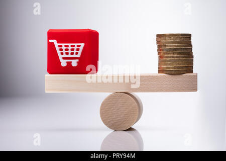 Red Shopping Cart Cubic Block And Stacked Coins Balancing On Wooden Seesaw Stock Photo