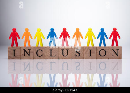 Multi Colored Human Figures Standing On Wooden Cubic Blocks Over Reflective Background Stock Photo