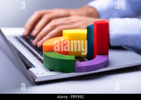 Businessperson's Hand Using Laptop With Colorful 3d Pie Chart On Keypad Stock Photo