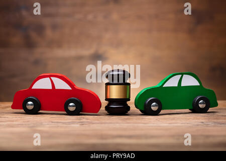 Wooden Mallet Between Two Red And Green Car On Wooden Surface Stock Photo