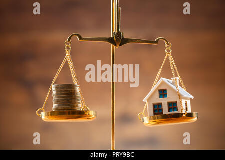 Close-up Of Stacked Coins And House Model Balancing On Golden Justice Scale Stock Photo