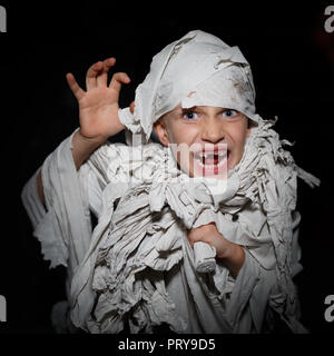 Boy wrapped in white bandages, like an Egyptian mummy, make faces on a black background Stock Photo
