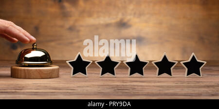 A Person's Hand Ringing Service Bell Near Black Five Star Rating Icon On Wooden Desk Stock Photo