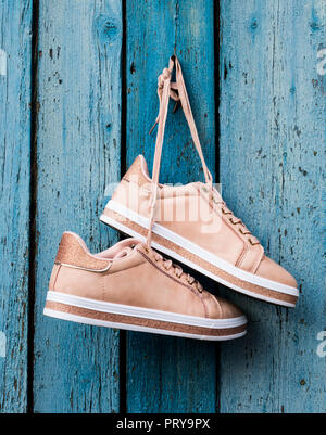 pair of beige fashionable female sports shoes hanging on a cord on a background of a blue old wooden wall Stock Photo