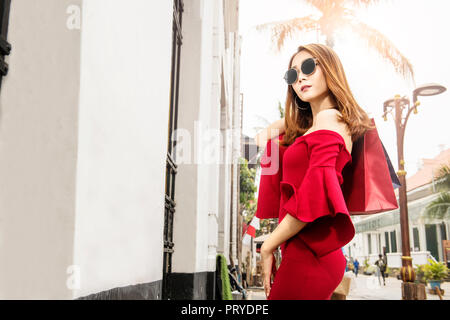 Pretty asian woman in red dress with shopping bags on the city street Stock Photo