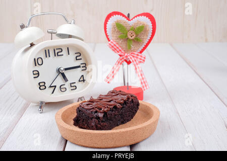 Alarm clock, note clipper and  chocolate brownie with melted chocolate on a wooden plate Stock Photo