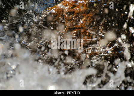 Beautiful, blurry and abstract background of white water drops falling on a brown-red rock surface, with light reflection effect and a lot of movement Stock Photo