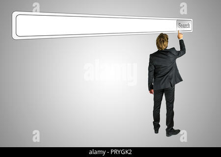 View from behind of a young businessman in a suit reaching up and touching a blank navigation Search bar angled obliquely across the top of the screen Stock Photo