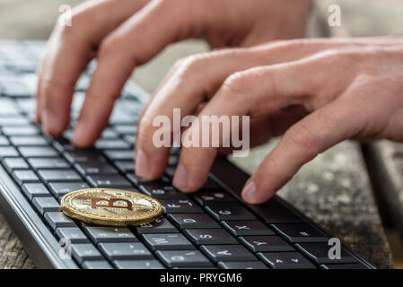 Golden Bitcoin coin or medallion over black computer keyboard and mans fingers typing bitcoin wallet password. Cryptocurrency security concept. Stock Photo