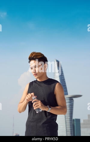 Young sports man opens a bottle of water teeth. The concept of sport and a healthy lifestyle. Stock Photo